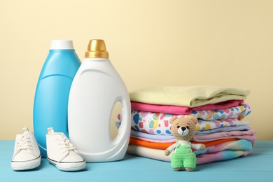 Photo of Bottles with fabric softeners, baby clothes and toy on light blue wooden table against beige background