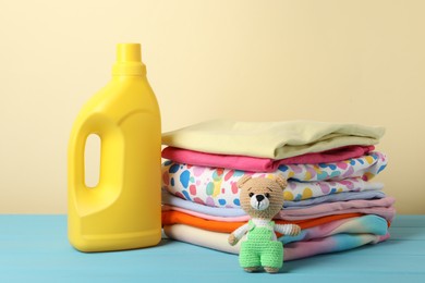 Photo of Bottle with fabric softener, baby clothes and toy on light blue wooden table against beige background