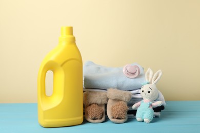 Photo of Bottle with fabric softener, baby clothes, pacifier and toy on light blue wooden table against beige background