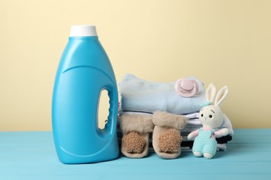 Photo of Bottle with fabric softener, baby clothes, pacifier and toy on light blue wooden table against beige background