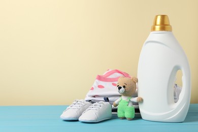 Photo of Bottle with fabric softener, baby clothes and toy on light blue wooden table against beige background. Space for text
