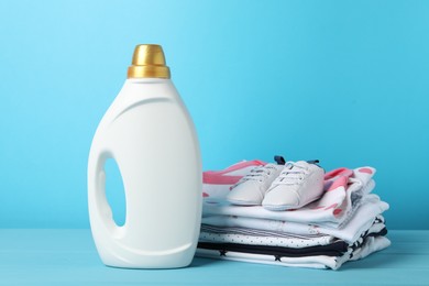 Photo of Bottle with fabric softener, baby clothes and shoes on light blue wooden table
