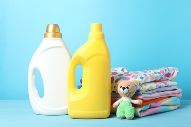 Photo of Bottles with fabric softeners, baby clothes and toy on light blue wooden table