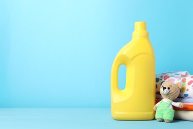 Photo of Bottle with fabric softener, baby clothes and toy on light blue wooden table. Space for text