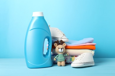 Photo of Bottle with fabric softener, baby clothes and toy on light blue wooden table