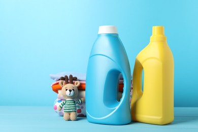 Photo of Bottles with fabric softeners, baby clothes and toy on light blue wooden table