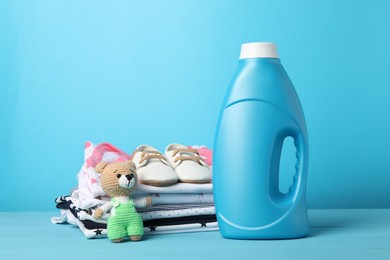 Photo of Bottle with fabric softener, baby clothes and toy on light blue wooden table