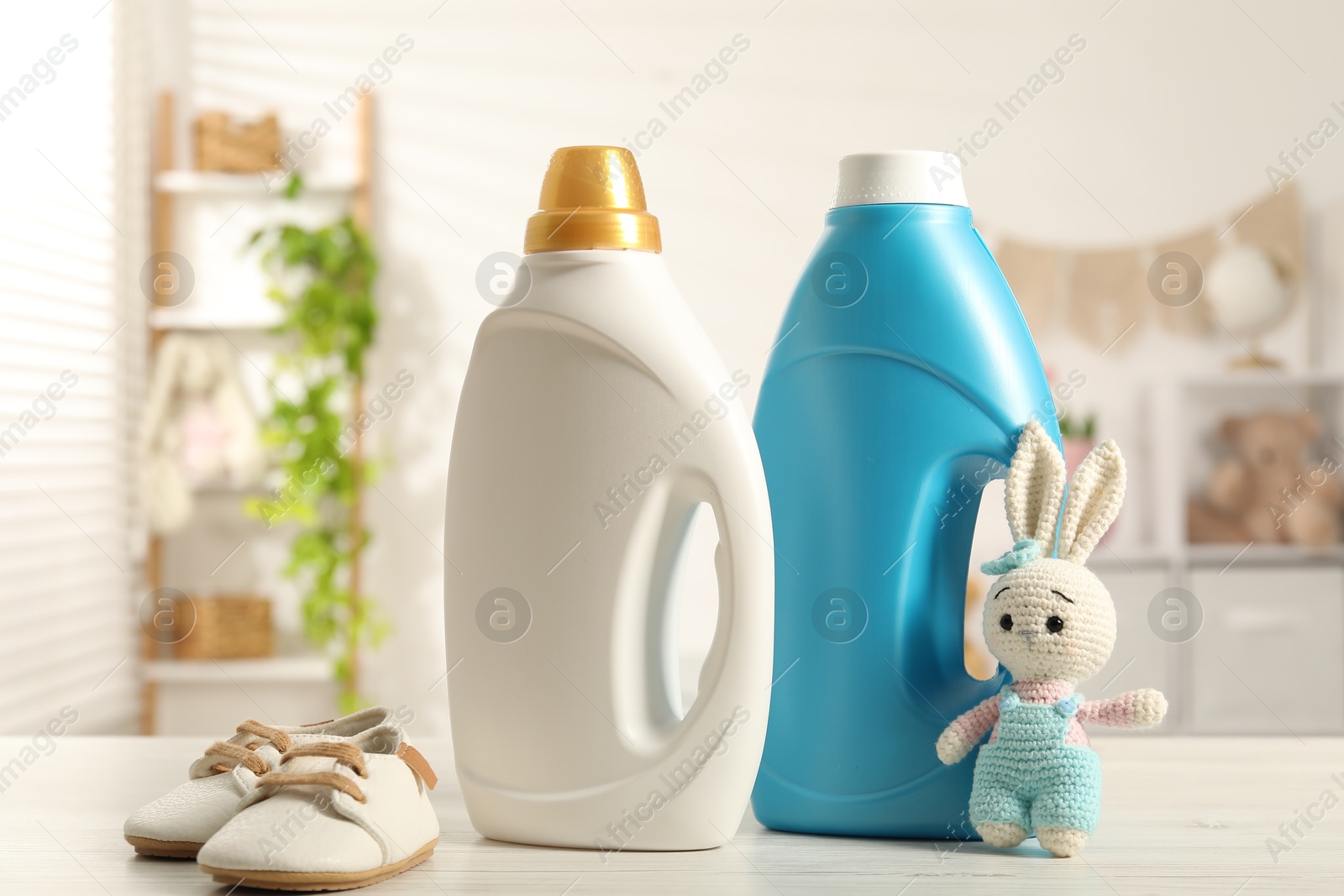 Bottles with fabric softeners, baby shoes and toy on light wooden table indoors Photo of Bottles with fabric softeners, baby shoes and toy on light wooden table indoors