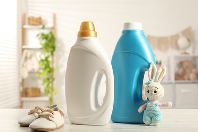 Photo of Bottles with fabric softeners, baby shoes and toy on light wooden table indoors