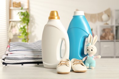 Photo of Bottles with fabric softeners, baby clothes and toy on light wooden table indoors