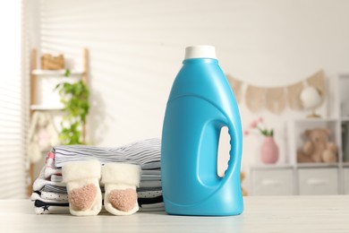 Photo of Bottle with fabric softener and stack of baby clothes on light wooden table indoors