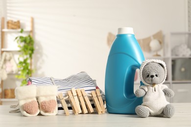 Photo of Bottle with fabric softener, baby clothes, clothespins and toy on light wooden table indoors