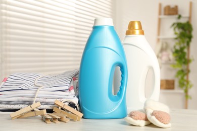 Photo of Bottles with fabric softeners, baby clothes and clothespins on light wooden table indoors