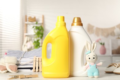 Photo of Bottles with fabric softeners, baby clothes, toy and clothespins on light wooden table indoors