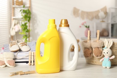 Photo of Bottles with fabric softeners, baby clothes and clothespins on light wooden table indoors
