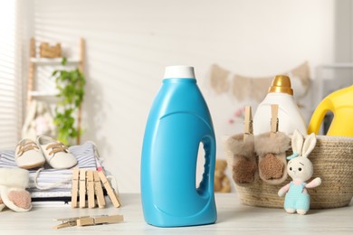 Photo of Bottles with fabric softeners, baby clothes, clothespins and toy on light wooden table indoors