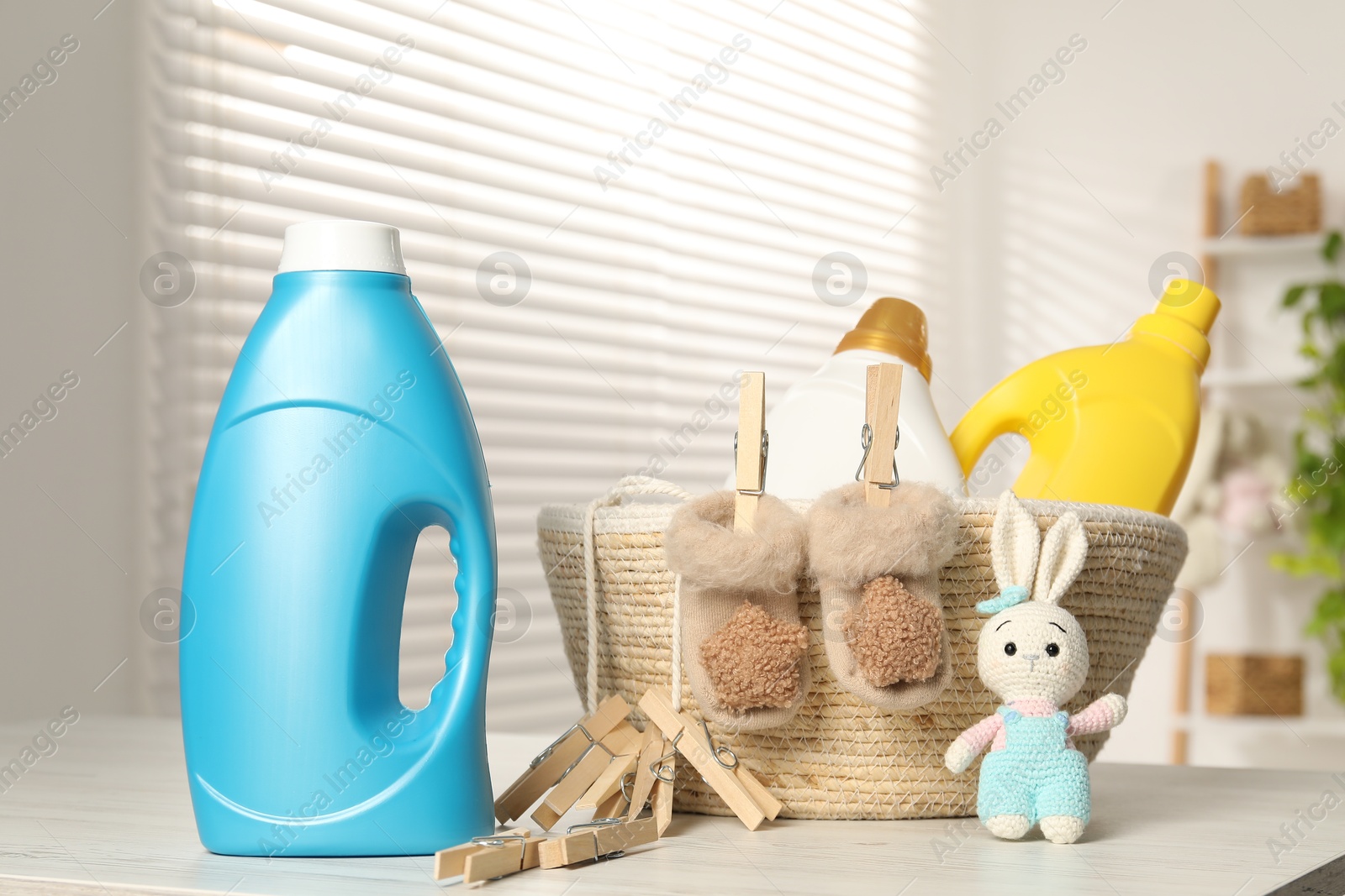 Bottles with fabric softeners, clothespins and toy on light wooden table indoors Photo of Bottles with fabric softeners, clothespins and toy on light wooden table indoors