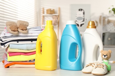 Photo of Bottles with fabric softeners, baby clothes and toy on light wooden table indoors