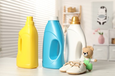 Photo of Bottles with fabric softeners, baby shoes and toy on light wooden table indoors