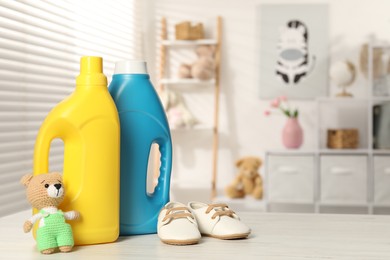 Photo of Bottles with fabric softeners, baby shoes and toy on light wooden table indoors. Space for text