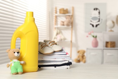 Photo of Bottle with fabric softener, baby clothes and toy on light wooden table indoors. Space for text