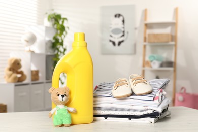 Photo of Bottle with fabric softener, stack of baby clothes and toy on light wooden table indoors