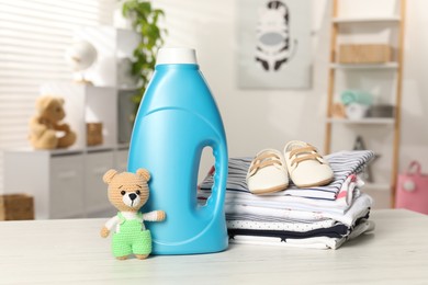 Photo of Bottle with fabric softener, stack of baby clothes and toy on light wooden table indoors