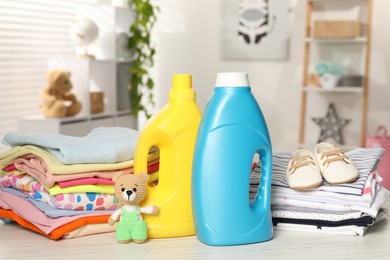 Photo of Bottles with fabric softeners, baby clothes and toy on light wooden table indoors