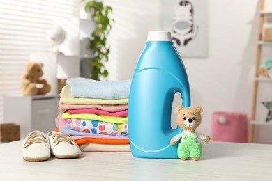 Photo of Bottle with fabric softener, stack of baby clothes and toy on light wooden table indoors