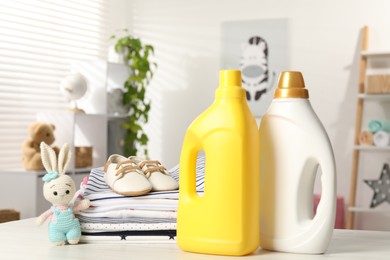 Photo of Bottles with fabric softeners, baby clothes and toy on light wooden table indoors