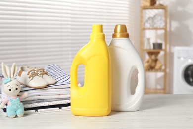 Photo of Bottles with fabric softeners, baby clothes and toy on light wooden table indoors