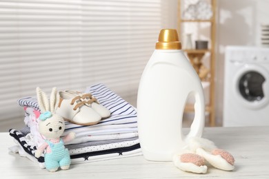 Photo of Bottle with fabric softener, baby clothes and toy on light wooden table indoors