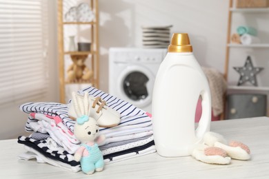 Photo of Bottle with fabric softener, baby clothes and toy on light wooden table indoors
