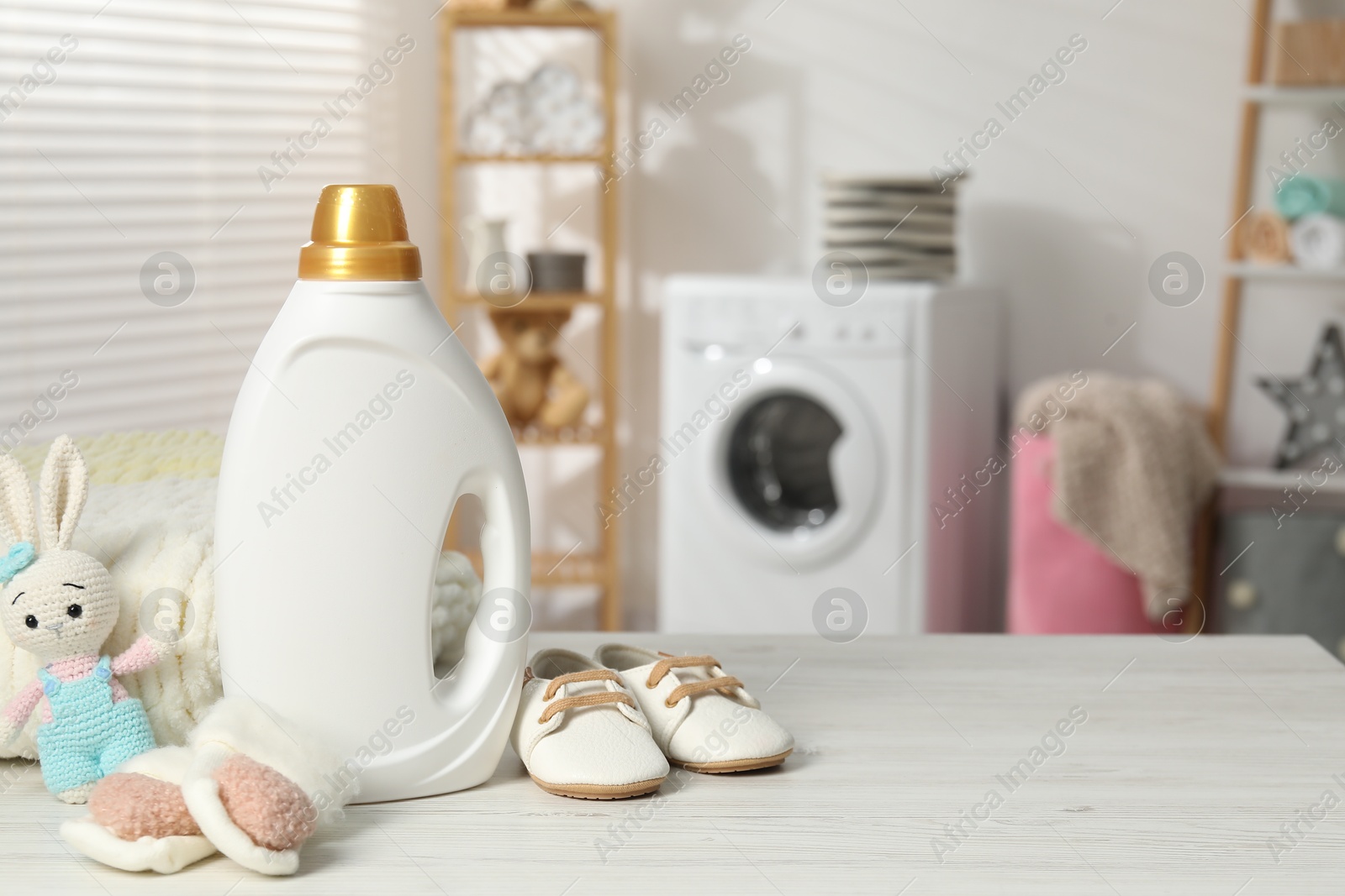 Bottle with fabric softener, baby shoes and toy on light wooden table indoors. Space for text Photo of Bottle with fabric softener, baby shoes and toy on light wooden table indoors. Space for text