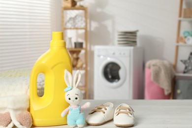 Photo of Bottle with fabric softener, baby shoes and toy on light wooden table indoors. Space for text