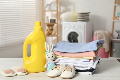 Photo of Bottle with fabric softener, baby clothes and toy on light wooden table indoors