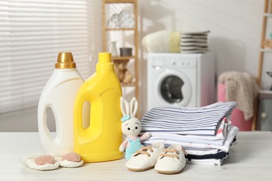 Photo of Bottles with fabric softeners, baby clothes and toy on light wooden table indoors