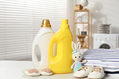 Photo of Bottles with fabric softeners, baby clothes and toy on light wooden table indoors