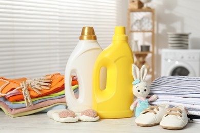 Photo of Bottles with fabric softeners, baby clothes, clothespins and toy on light wooden table indoors