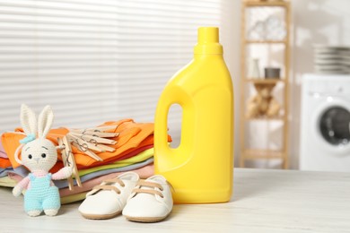 Photo of Bottle with fabric softener, baby clothes, clothespins and toy on light wooden table indoors