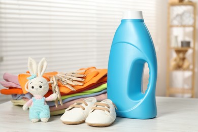 Photo of Bottle with fabric softener, baby clothes, clothespins and toy on light wooden table indoors
