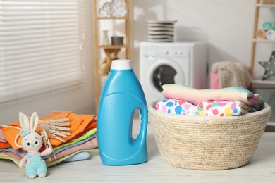Photo of Bottle with fabric softener, baby clothes, clothespins and toy on light wooden table indoors