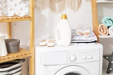 Photo of Bottle with fabric softener and baby clothes on washing machine indoors