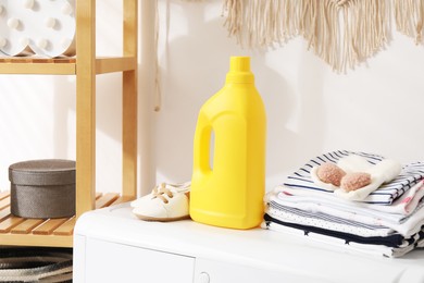 Photo of Bottle with fabric softener and baby clothes on washing machine indoors