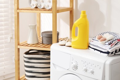 Photo of Bottle with fabric softener and baby clothes on washing machine indoors