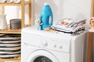 Photo of Bottle with fabric softener, baby clothes, clothespins and toy on washing machine indoors