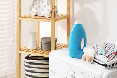 Photo of Bottle with fabric softener, baby clothes and toy on washing machine indoors
