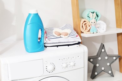 Photo of Bottle with fabric softener and baby clothes on washing machine indoors