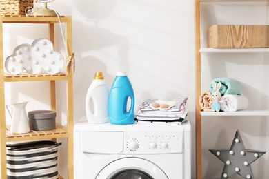 Photo of Bottles with fabric softeners and baby clothes on washing machine indoors
