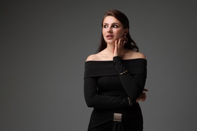 Photo of Young woman in stylish black dress on grey background, space for text
